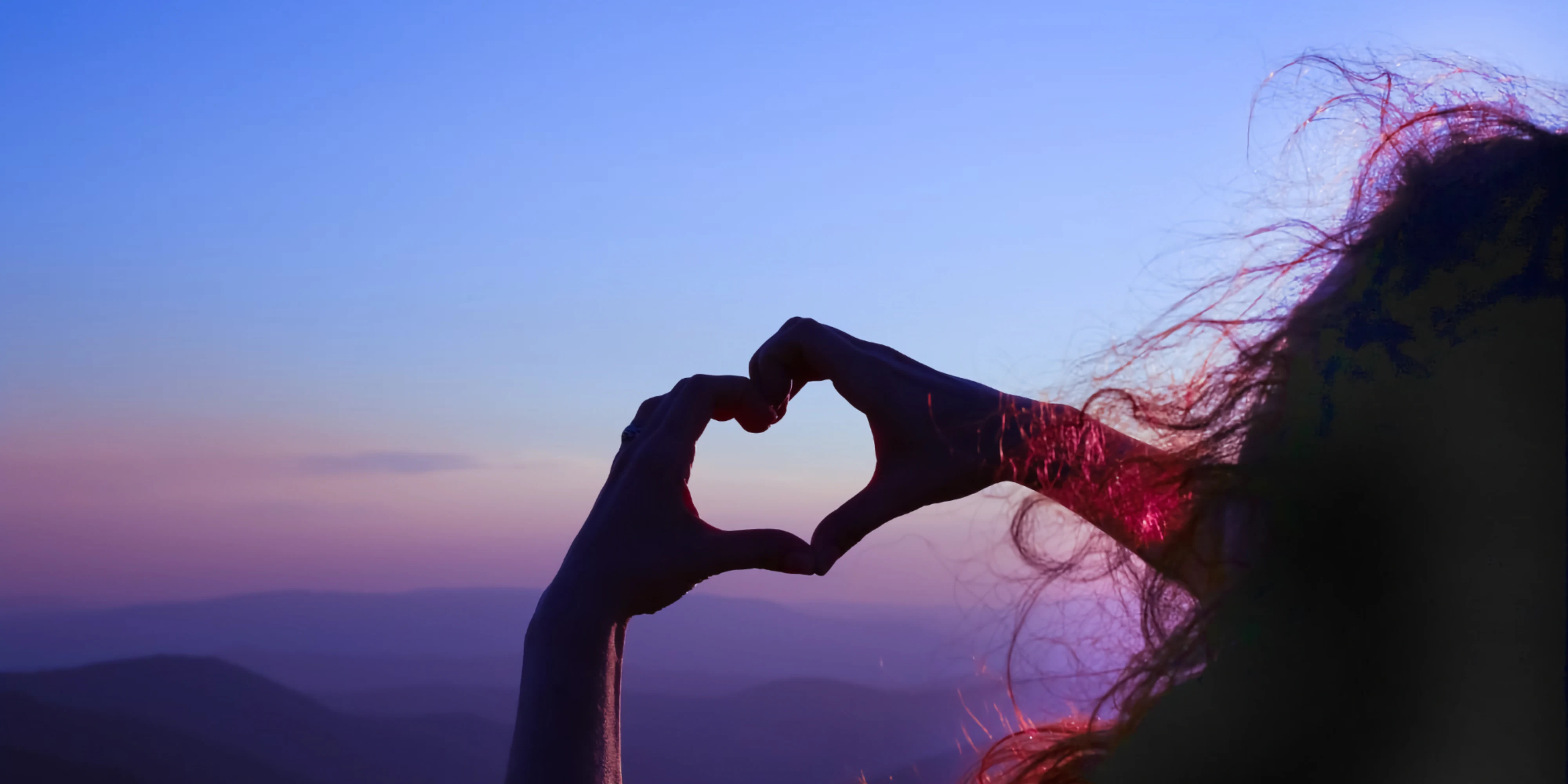 Heart shape made with hands against a skyline.