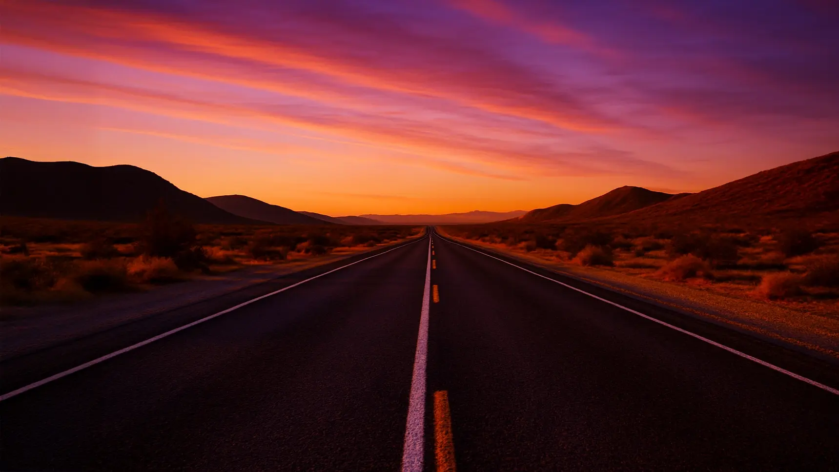 Road stretching into horizon with an orange and purple sunset 